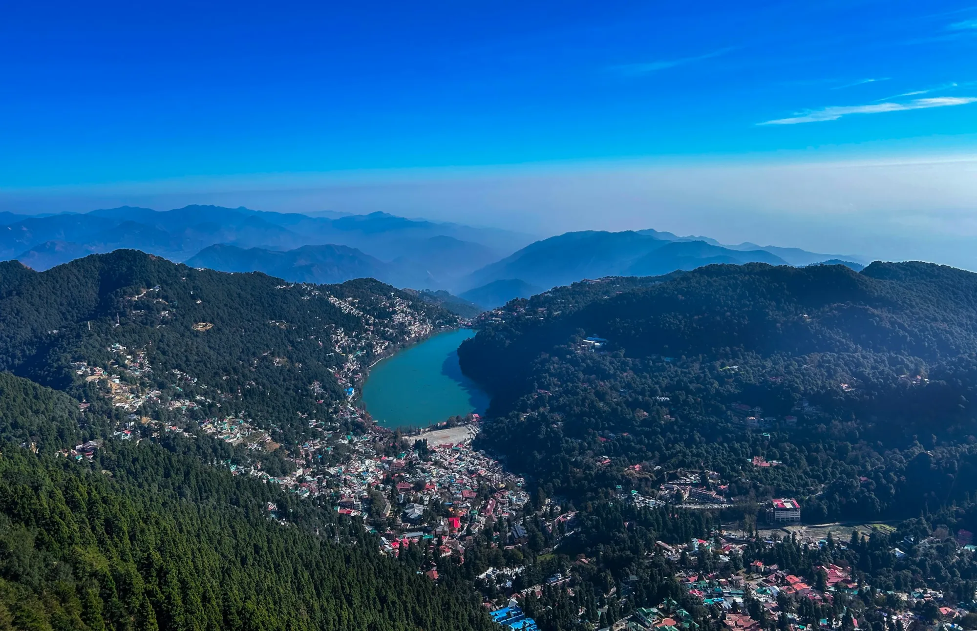 Naini Lake and Nainital town seen from a hilltop, surrounded by forested mountains